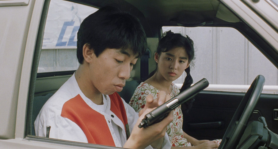 Masaki inspects the smuggled gun as Sayaka looks on